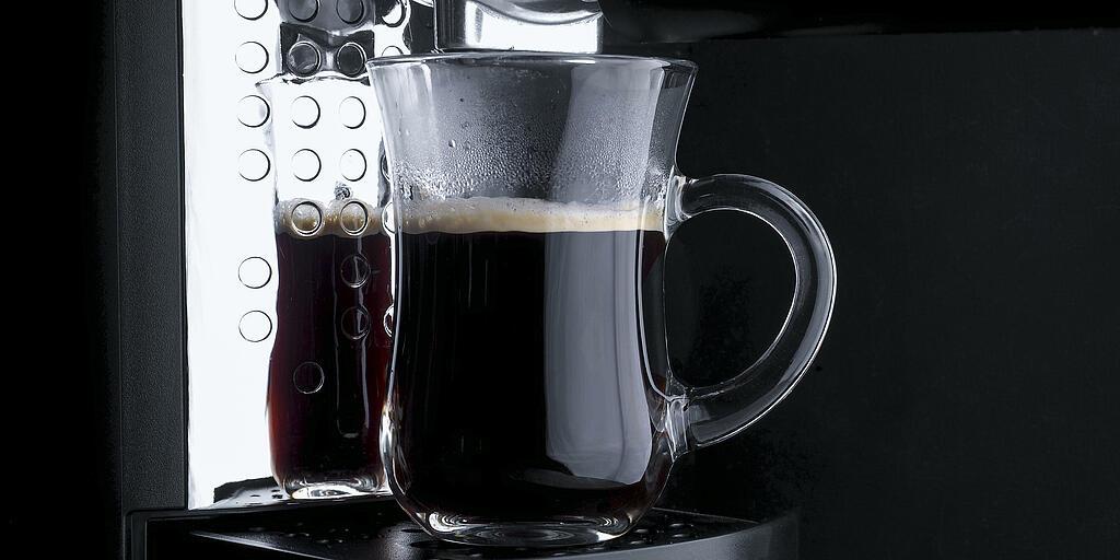 Eine durchsichtige Tasse wird von einer Kaffeemaschine befüllt