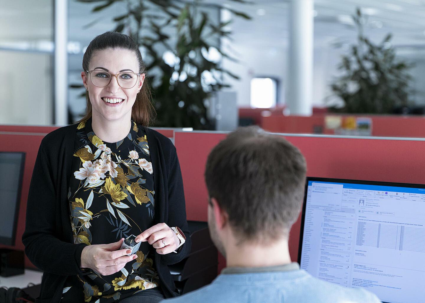 Frau steht neben Mitarbeiter im Büro und lacht in die Kamera