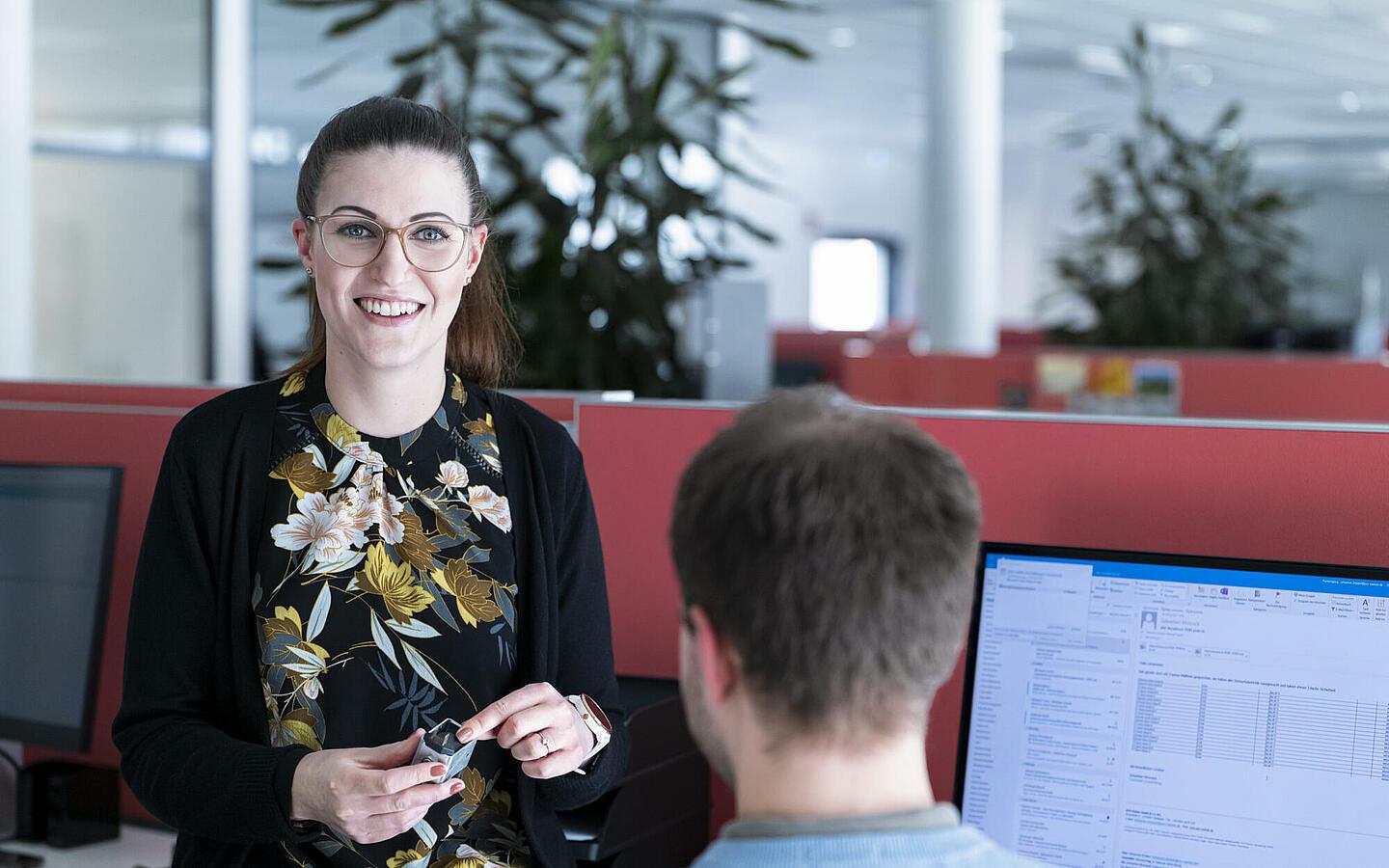 Frau steht neben Mitarbeiter im Büro und lacht in die Kamera