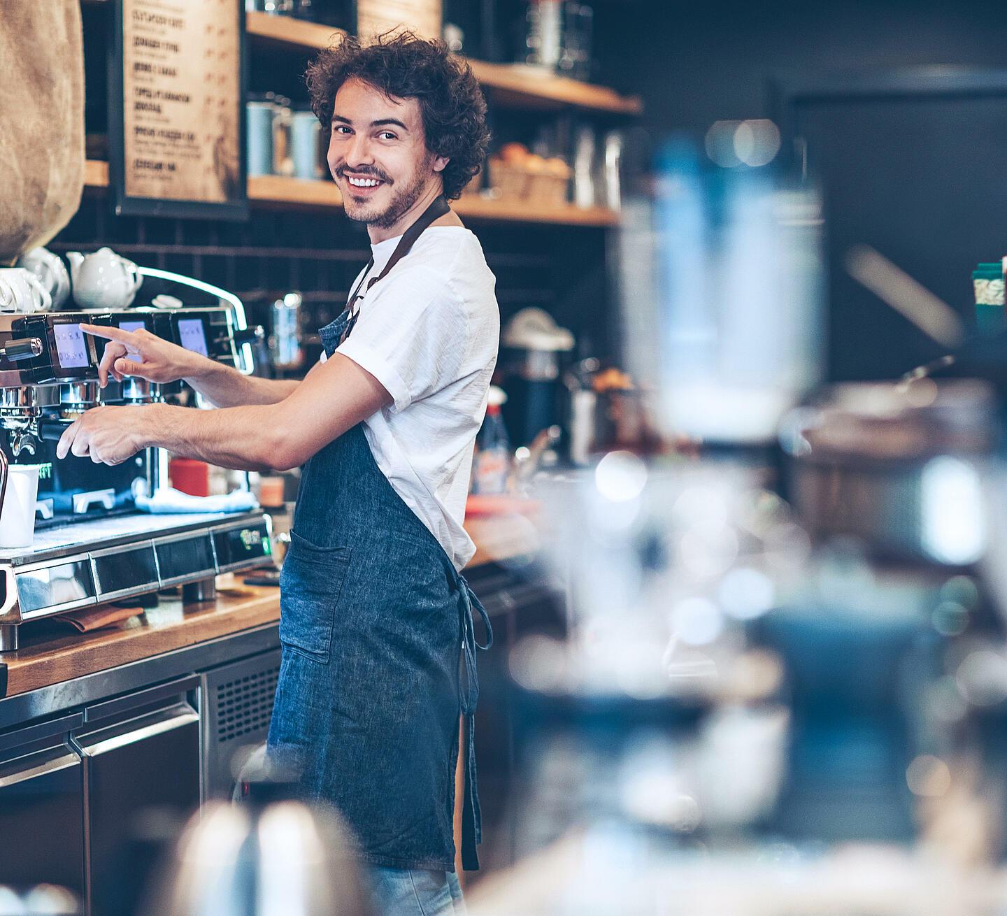 Ein Mann steht hinter der Theke in einem Cafe und macht einen Kaffee an der Maschine