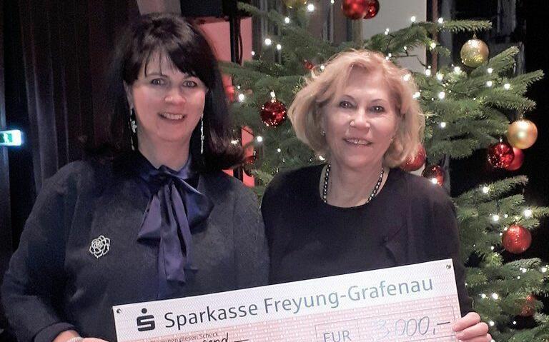Due donne presentano un assegno di donazione davanti a un albero di Natale