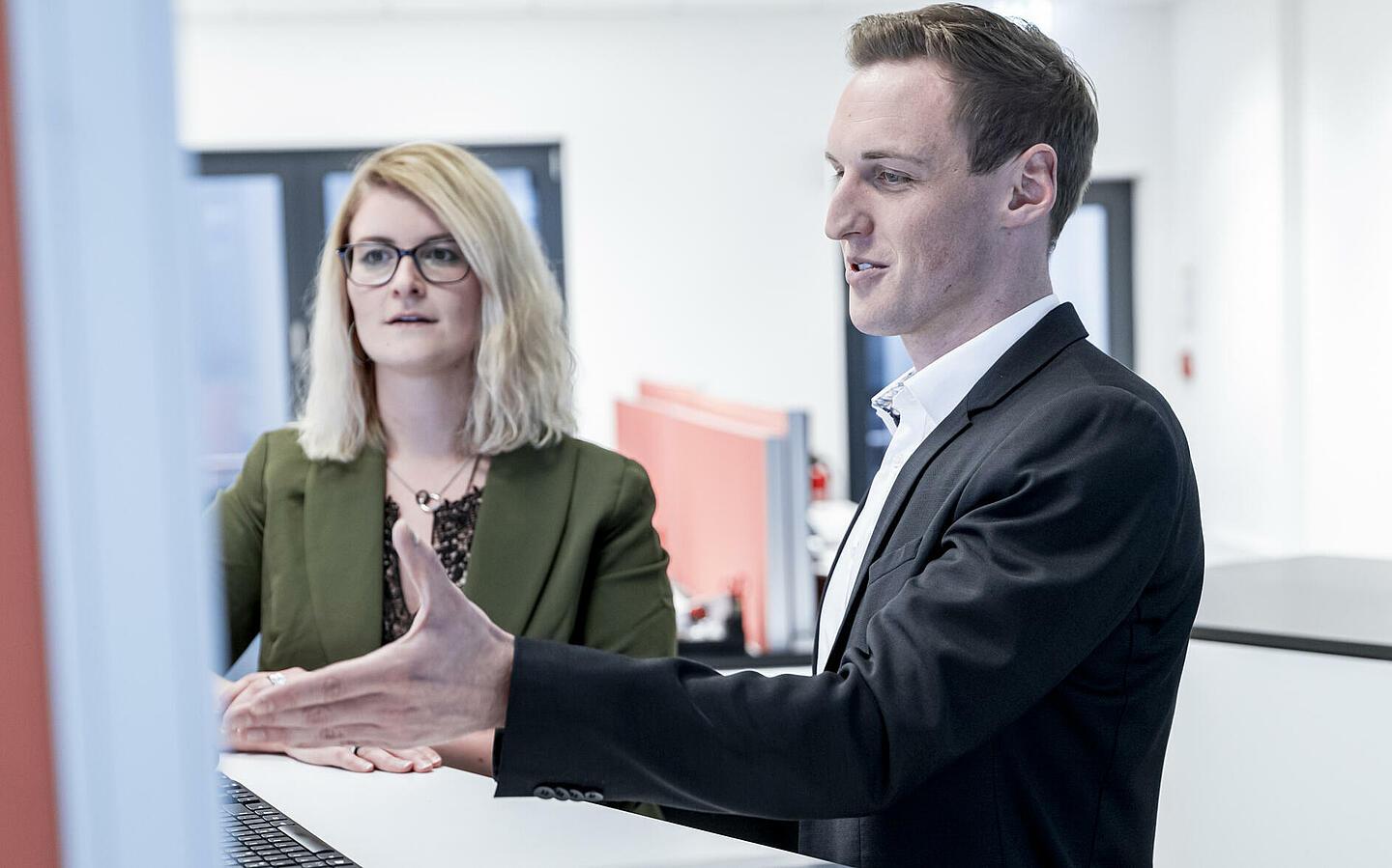 Zwei Mitarbeiter stehen hinter einem Computer und schauen auf den Bildschirm