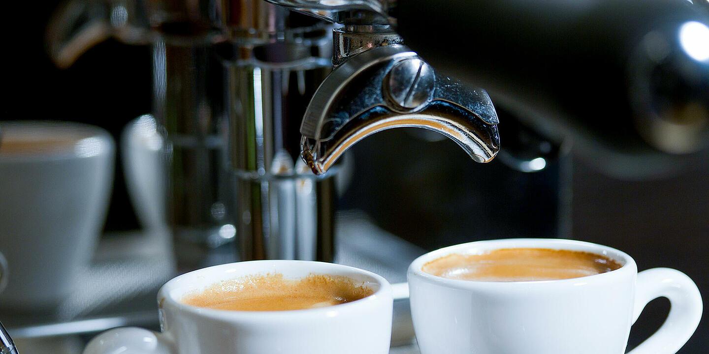 Dos tazas llenas junto a una cafetera plateada