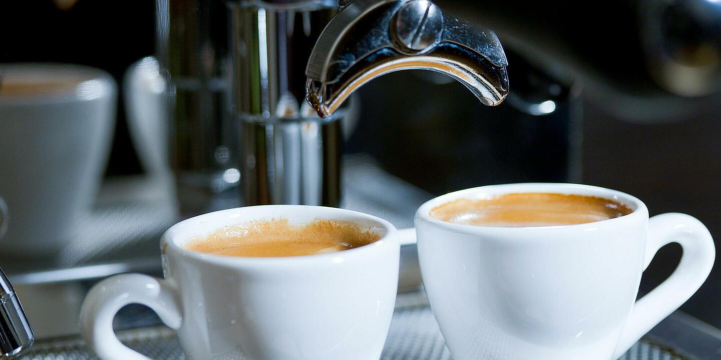 Unter einer silbernen Kaffeemaschine stehen zwei volle Tassen