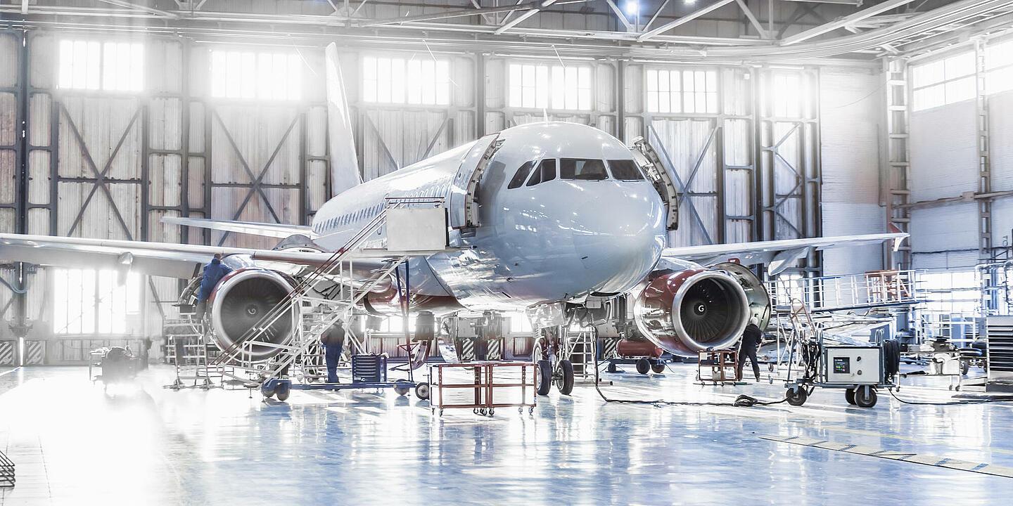 In einer großen Halle steht ein Flugzeug, an dem Personen arbeiten.