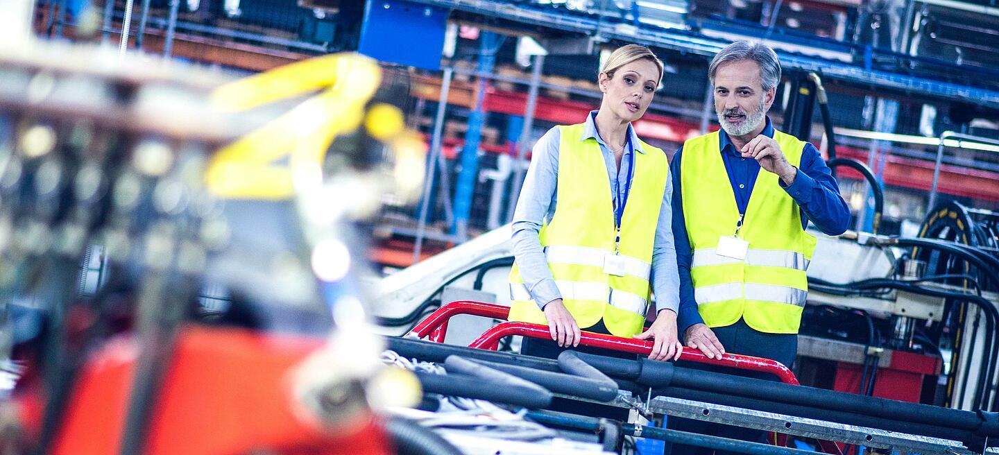 Zwei Personen mit Warnwesten sehen sich eine Maschine an